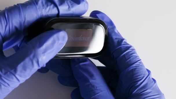 Крупный план электронного импульсного оксиметра в руках врача в синих латексных перчатках — стоковое видео