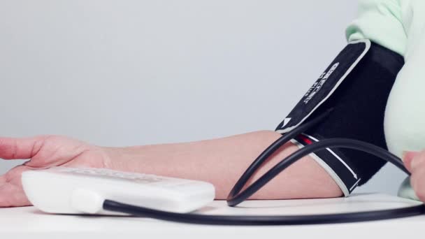 Adulto o una mujer anciana mide la presión arterial con un tonómetro digital portátil en casa. — Vídeo de stock