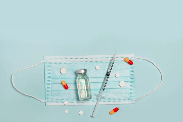 Syringe with medicine from glass vial , medical mask and color pills on blue background, flat lay, copyspace. Vaccination against influenza, covid 19, measles, coronavirus disease. Vaccination and immunization concept