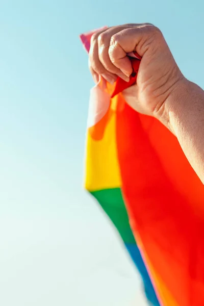 Main d'homme avec drapeau arc-en-ciel volant au soleil brillant sur fond de ciel bleu — Photo