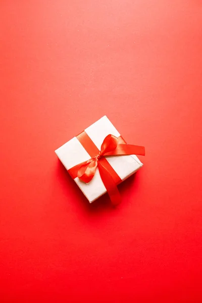 Tarjeta de felicitación de San Valentín con caja de regalo roja y lazo de cinta decorado sobre fondo rojo — Foto de Stock