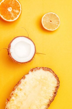 Parlak sarı arka planda çeşitli egzotik meyveler. Yarım limon, portakal, ananas ve hindistan cevizi. Üst görünüm, dikey, düz uzanma