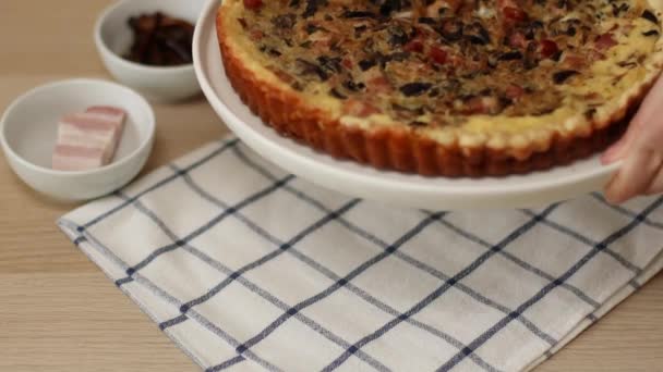 Homemade open pie with bacon, mushrooms and onions on the table. Female hands put a dish with tart pie on the table — Stock Video