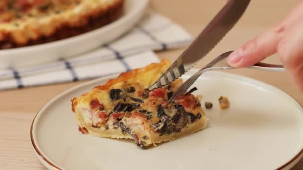 Primer plano de tomar bocado de pastel casero rebanada con tocino, champiñones y cebollas, pollo, comer con tenedor en la mesa. Comer delicioso quiche lorraine — Vídeo de stock