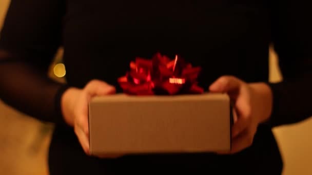 Manos femeninas dando un regalo de regalo en papel kraft a cuadros con gran lazo rojo. Feliz Navidad o Feliz Año Nuevo 2022. Persona que sostiene la caja para el cumpleaños — Vídeo de stock