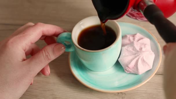 Versare il caffè turco in tazza su un tavolo di legno. Persona di sesso maschile che prepara caffè mattutino. Delizioso marshmallow ai mirtilli soffiati su un piattino — Video Stock
