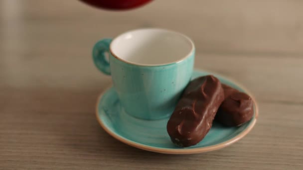 Café negro caliente aromático en taza de cerámica y dulces de chocolate. Verter café negro en taza azul de la cafetera turca en la mesa de madera — Vídeo de stock
