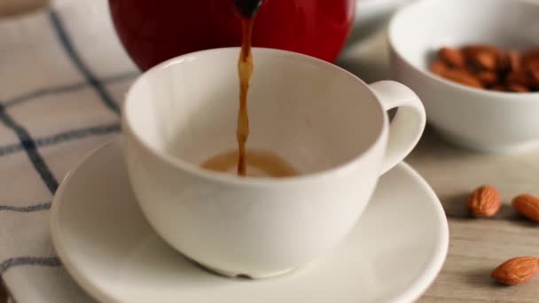 Café negro vertiendo en taza de porcelana blanca. Almendras en un bol sobre la mesa — Vídeo de stock