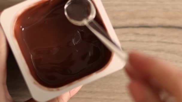 Vrouw hand nemen lepel een chocolade mousse of pudding in plastic pot — Stockvideo
