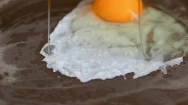 Tojást sütni egy serpenyőben egy forró tűzhelyen. Törött tojás beleesik a serpenyőbe.. — Stock videók
