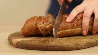Kadın ekmek bıçağıyla ahşap mutfak tahtasına çavdar ekmeği dilimliyor.