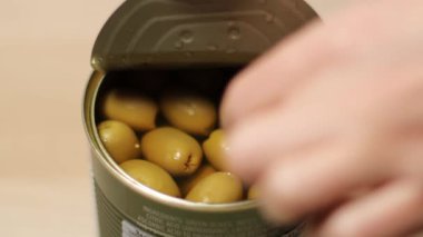 Erkek eli teneke kutudan büyük yeşil bir zeytin çıkarır.