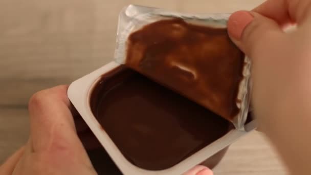 Man mão abre recipiente de plástico com mousse de chocolate ou pudim na mesa de madeira — Vídeo de Stock