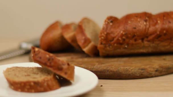 Dilimlenmiş çavdar ekmeği, tabakta tohumlar ve ahşap mutfak tahtasının üzerinde bir somun ekmek. — Stok video