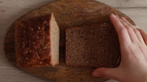 Close-up van de man die een stuk brood neemt. Hand neemt verse sneetjes gesneden brood op houten plank — Stockvideo