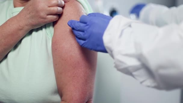Pielęgniarka lub lekarz noszący rękawicę medyczną wstrzykuje szczepionkę przeciw koronawirusowi lub inną szczepionkę w ramię starszego pacjenta.. — Wideo stockowe