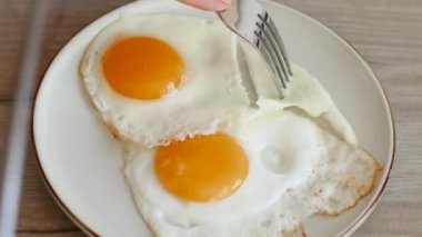 Beyaz bir tabakta duran kızarmış yumurtalar mutfak bıçağıyla parçalara ayrılır..