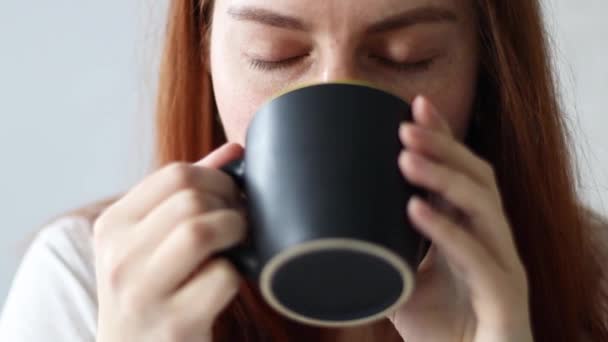 Blank meisje met lang haar drinken warm latte koffie uit zwart kopje genieten ochtend ontbijt — Stockvideo