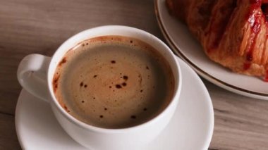 Hafif ahşap masa arkaplanının üzerinde küçük beyaz bir fincanda Espresso kahvesi. Çilekli taze Fransız kruvasanı.