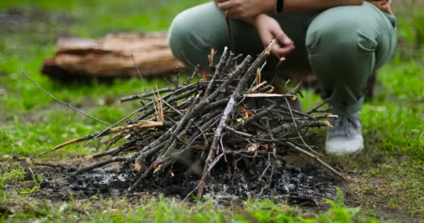 Kibriti olan genç bir kadın ormanda kamp ateşi için bir dal yakıyor. — Stok video