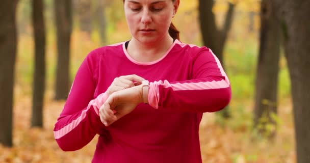 Frau mit Fitness-Tracker am Handgelenk auf der Straße im Stadtpark. Goldener Saison-Ahorn hinterlässt abgefallenen Teppich auf dem Boden. Herbst — Stockvideo