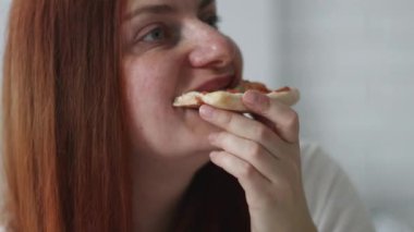 Evdeki kanepede otururken İtalyan pizzası yiyen beyaz kadının yakın plan portresi.