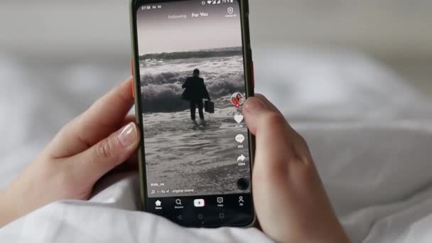 Oekraïne - 28 februari 2021: Meisje kijken naar video 's in populaire Tiktok toepassing op zwarte smartphone. — Stockvideo