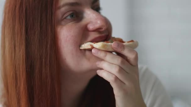 Närbild porträtt av kaukasisk kvinna äter välsmakande italienska skiva pizza när du sitter på soffan i hemmet — Stockvideo