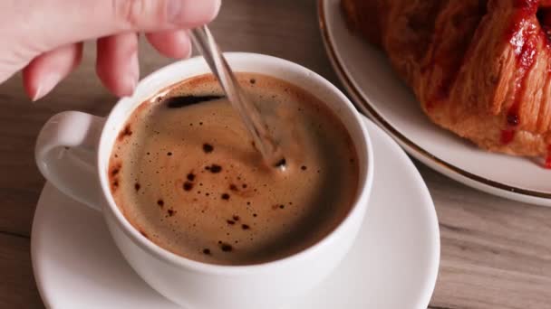 Ein Mann rührt Zucker in einer Tasse aromatischen Kaffees mit einem Glaslöffel auf einem Holztisch an — Stockvideo