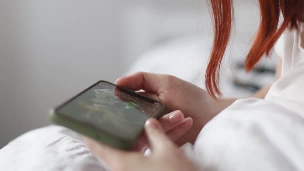 Mujer de la mano sosteniendo el teléfono inteligente y viendo vídeo en una cama dentro de casa en interiores — Vídeo de stock