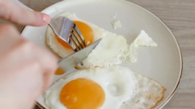 Beyaz bir tabakta duran kızarmış yumurtalar mutfak bıçağıyla parçalara ayrılır. Sabah kahvaltısı. Geleneksel kahvaltı