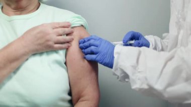 Tıbbi eldiven giyen hemşire ya da doktor yaşlı bir hastanın koluna koronavirüs aşısı ya da başka bir aşı enjekte ediyor..