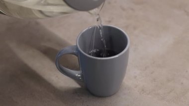 Gri bardakta sıcak çay içirmek için çaydanlıktan kaynar su döken adam..