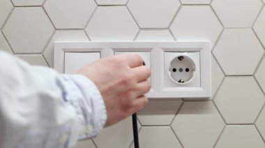 Erkek el prizden elektrik fişini çekiyor. Dünya Saati elektrik enerjisinden tasarruf ediyor