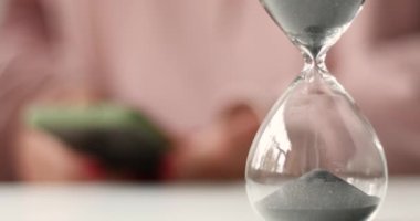 İş kadını ya da öğrenci işyerinde cep telefonu kullanıyor. Testi geçmek, uzaktan çalışma konsepti kum saati ölçme, erteleme.