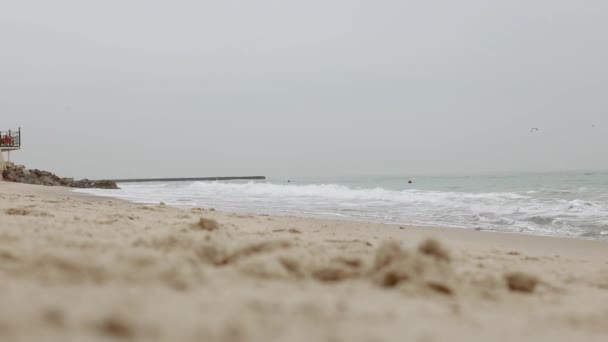 Winterstrand mit Spritzwasser. Die Meereswelle kracht gegen den Steinstrand. See mit stürmischen Wellen an bewölkten, kalten Wintertagen. — Stockvideo