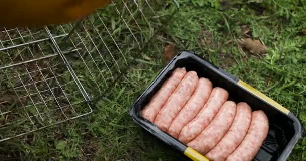 Man lägger råa korvar på grillen. Grillad färsk köttkorv. — Stockvideo