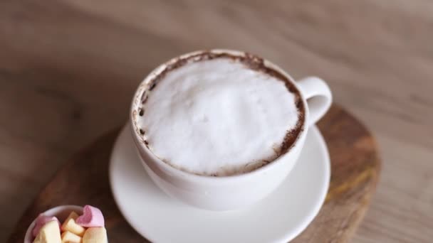 Капучино кофе в керамической чашке с воздухом любви зефир конфеты на деревянной доске. Домашний кофе. Вкусный завтрак — стоковое видео