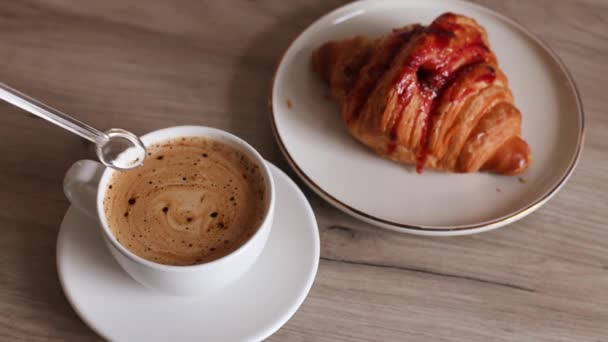 Πεντανόστιμο γαλλικό κρουασάν με γέμιση φράουλας και αρωματικό καφέ σε ξύλινο τραπέζι. Ανάδευση προσώπου χέρι καφέ με κουτάλι — Αρχείο Βίντεο
