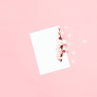 Blank paper card mockup with cherry flower and copy space on a pink background. Minimal business template. Flat Lay, top view.