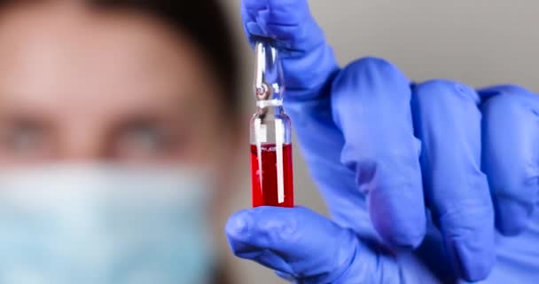 Lekarz w ochronnych rękawiczkach chirurgicznych trzyma ampułkę z czerwonym płynem i strzykawkę do wstrzykiwań z chorobą cukrzycową — Wideo stockowe
