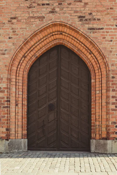 Old wooden arch doors of an ancient castle and a red brick wall of a building