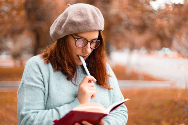 Estudante bonito escrevendo notas no caderno sentado ao ar livre no parque da natureza — Fotografia de Stock
