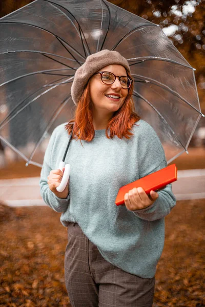 Χαμογελαστή κοπέλα με γυαλιά και διάφανη ομπρέλα στο πάρκο. Φοιτητής κολεγίου χαλαρώνοντας στον κήπο φθινόπωρο — Φωτογραφία Αρχείου