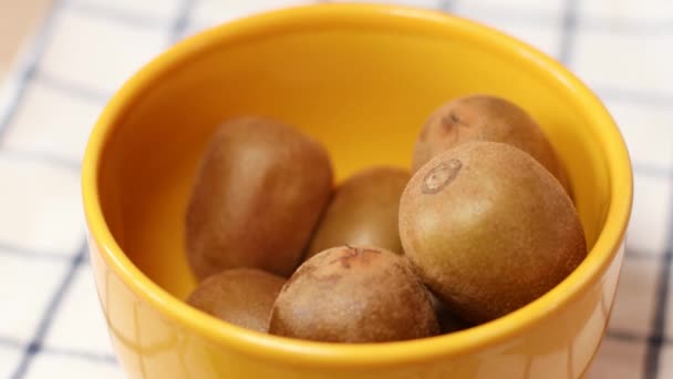 Primo piano di mano femminile mette kiwi frutta in ciotola gialla sul tavolo della cucina. — Video Stock