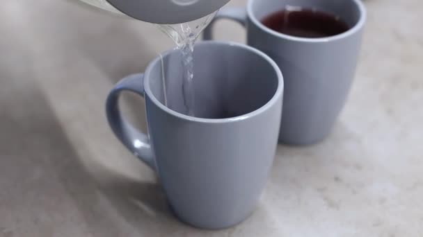 Hombre vertiendo agua hirviendo de la tetera para hacer bebida de té caliente en taza gris. — Vídeos de Stock