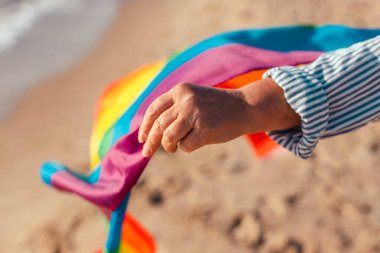 LGBT eşit haklar hareketi ve cinsiyet eşitliği kavramı. Mavi arka planda renkli bir gökkuşağı bayrağı olan genç bir el..