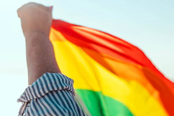 Mavi arka planda renkli bir gökkuşağı bayrağı olan genç bir el. LGBT eşit haklar hareketi ve cinsiyet eşitliği kavramı — Stok fotoğraf