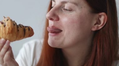 Uzun saçlı genç kız çikolatalı taze kruvasan yiyor ve sabah kahvaltısının tadını çıkarıyor.