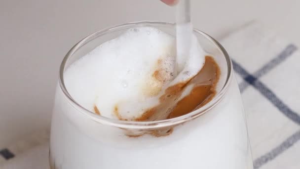 여자 손 이 커피와 우유, 캐러멜을 집 식탁에 놓인 유리 숟가락 과 혼합 한다 — 비디오